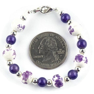 May include: A purple and white beaded bracelet with a silver clasp. The bracelet is about the size of a UK 20 pence coin.