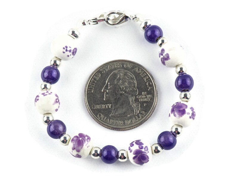 May include: A purple and white beaded bracelet with a silver clasp. The bracelet is about the size of a UK 20 pence coin.