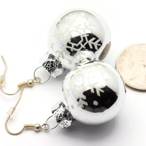 May include: Silver Christmas ornament earrings with snowflake designs. The ornaments are about the size of a quarter.