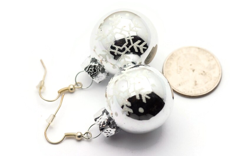 May include: Silver Christmas ornament earrings with snowflake designs. The ornaments are about the size of a quarter.