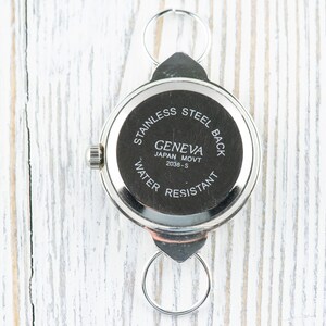 Peut inclure: Le dos d'une montre argent&eacute;e avec un bo&icirc;tier rond et un fond &agrave; enclenchement. Le cadran de la montre indique "Geneva Japan Movt 2039-S" et "Stainless Steel Back Water Resistant".