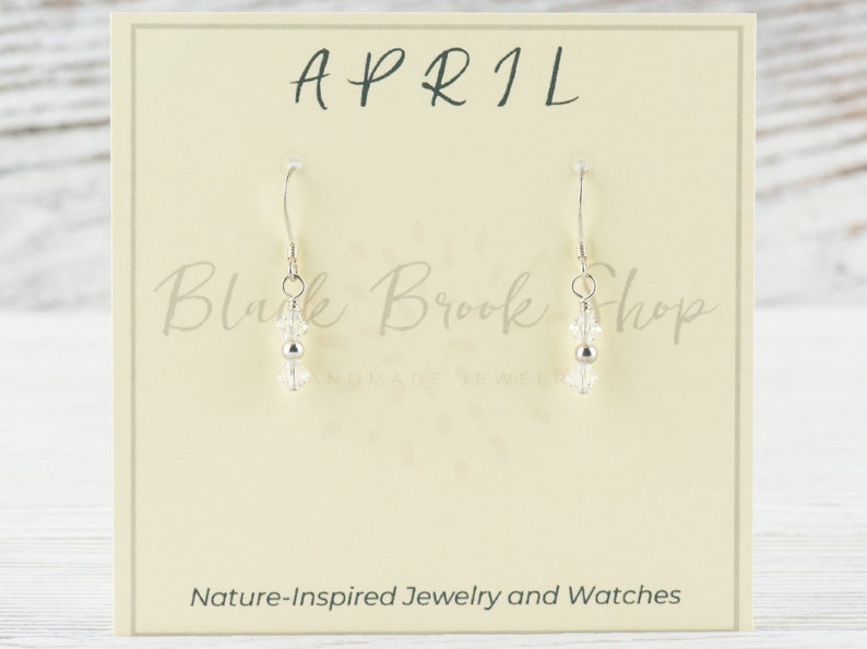 May include: Silver earrings with clear crystal beads and a silver bead. The earrings are on a white card with the text "APRIL" and "Black Brook Shop Handmade Jewelry".