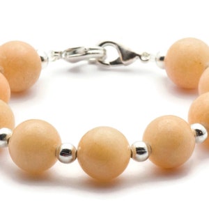 Puede incluir: Un brazalete hecho de cuentas de color naranja claro con detalles plateados. El brazalete tiene un cierre de broche.