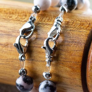 May include: Close-up of a silver clasp on a beaded necklace with pink and grey stones.