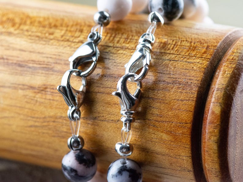 May include: Close-up of a silver clasp on a beaded necklace with pink and grey stones.