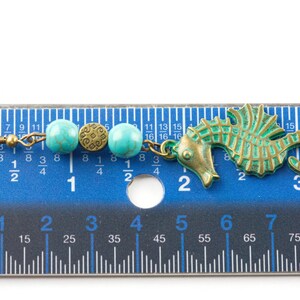 May include: A turquoise and brass seahorse earring with turquoise beads and a brass charm. The earring is measured against a ruler, showing it is approximately 5 cm long.