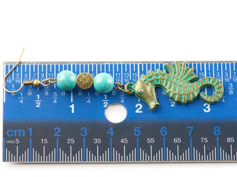 May include: A turquoise and brass seahorse earring with turquoise beads and a brass charm. The earring is measured against a ruler, showing it is approximately 5 cm long.