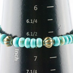 May include: Turquoise and gold beaded bracelet measuring 6 1/2 inches on a measuring tape.
