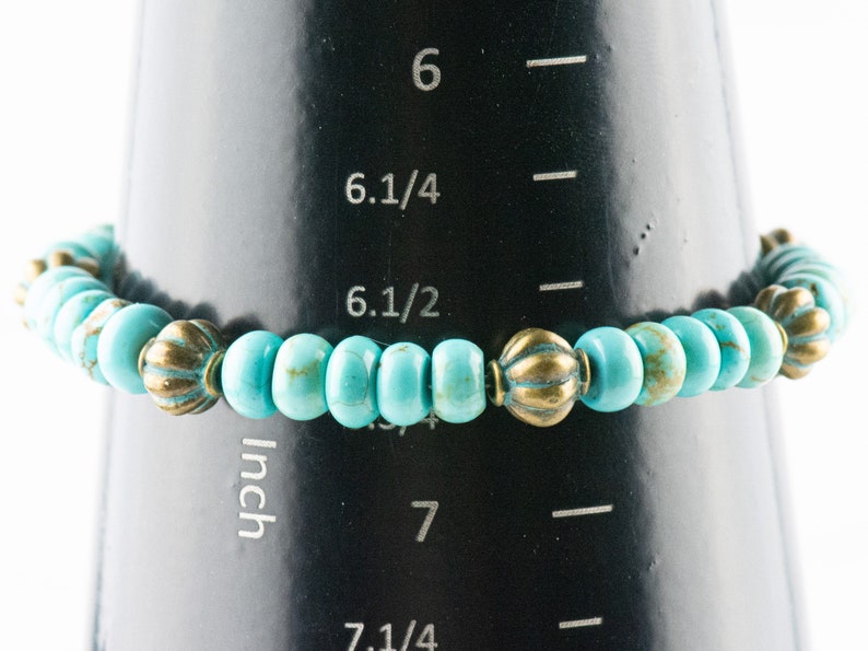 May include: Turquoise and gold beaded bracelet measuring 6 1/2 inches on a measuring tape.