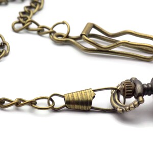 Pode incluir: Um rel&oacute;gio de bolso dourado com um design ornamentado e uma corrente anexada. A corrente tem um fecho para prender &agrave; roupa.