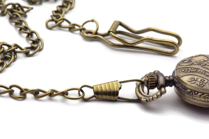 Pode incluir: Um rel&oacute;gio de bolso dourado com um design ornamentado e uma corrente anexada. A corrente tem um fecho para prender &agrave; roupa.