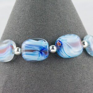 May include: A bracelet made with blue and white glass beads with silver spacer beads. The beads have a swirling pattern.