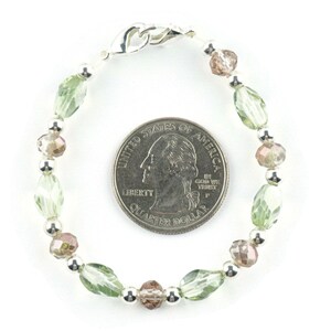 May include: A green and brown beaded bracelet with a silver clasp. The bracelet is about the size of a UK 20 pence coin.