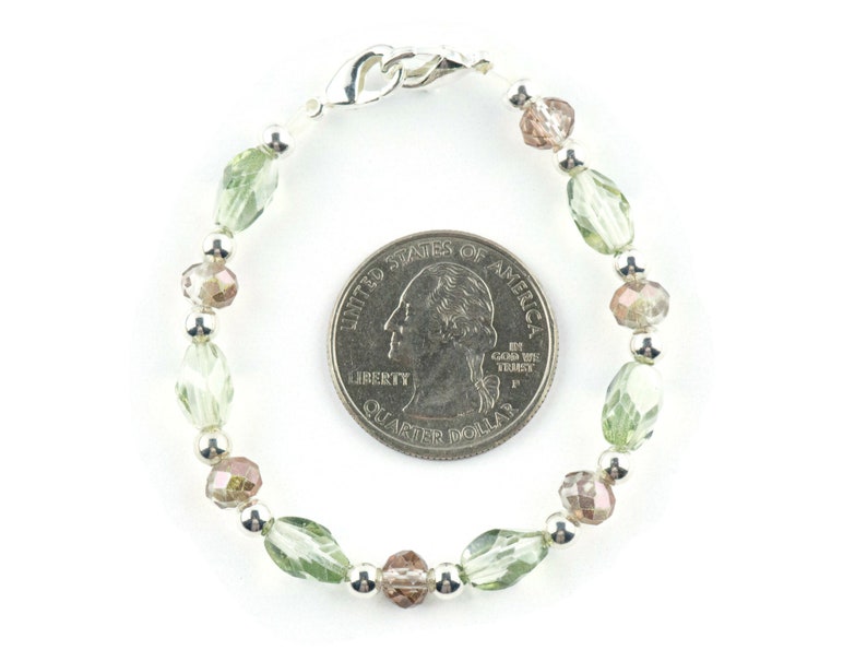 May include: A green and brown beaded bracelet with a silver clasp. The bracelet is about the size of a UK 20 pence coin.