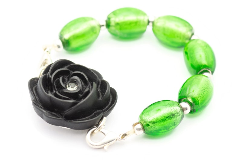 May include: A black rose charm bracelet with green glass beads. The rose has a small rhinestone in the center.