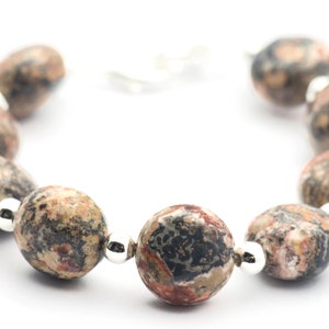 May include: A bracelet made of brown, black, and white speckled oval-shaped beads with silver spacers.