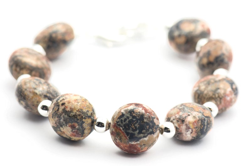 May include: A bracelet made of brown, black, and white speckled oval-shaped beads with silver spacers.