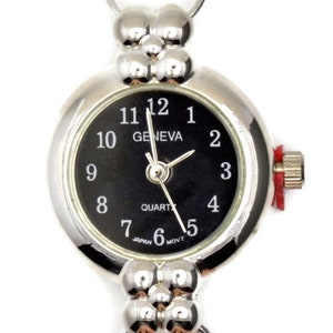 Könnte beinhalten: Eine silberfarbene Uhr mit schwarzem Zifferblatt und weißen Zahlen. Die Uhr hat ein rundes Zifferblatt und ein silbernes Armband mit einem Verschluss. Das Zifferblatt der Uhr zeigt "Geneva Quartz" und hat einen roten Sekundenzeiger.