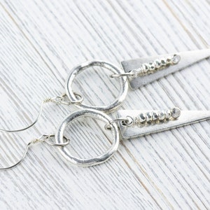 May include: A pair of silver earrings with a hammered metal circle and a triangular pendant with a row of silver beads.