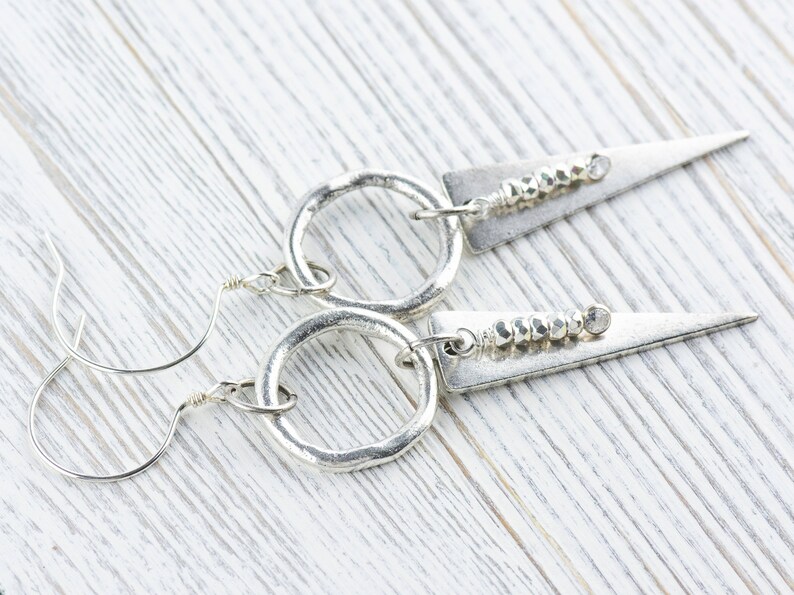 May include: A pair of silver earrings with a hammered metal circle and a triangular pendant with a row of silver beads.