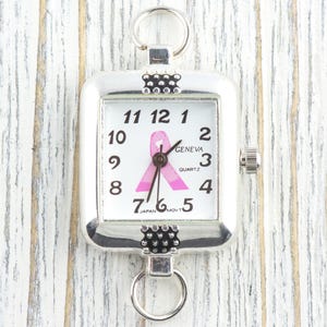 Pu&ograve; includere: Orologio al quarzo quadrato color argento con quadrante bianco con numeri neri e un nastro rosa. L'orologio ha anelli nella parte superiore e inferiore per il fissaggio. Il quadrante recita "GENEVA QUARTZ JAPAN MOV'T".