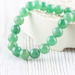 May include: A green jade stone bracelet with round beads. The bracelet is on a white surface.