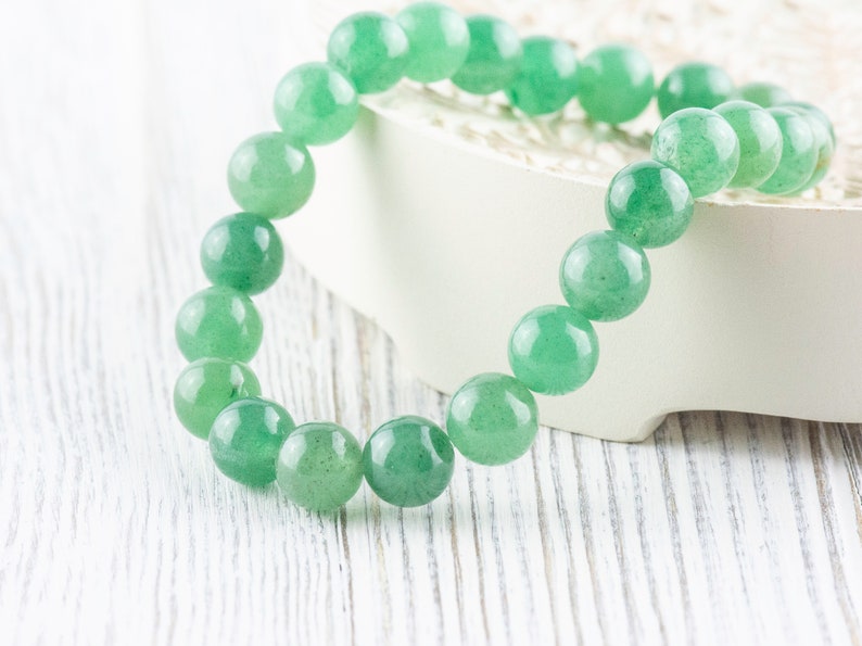 May include: A green jade stone bracelet with round beads. The bracelet is on a white surface.