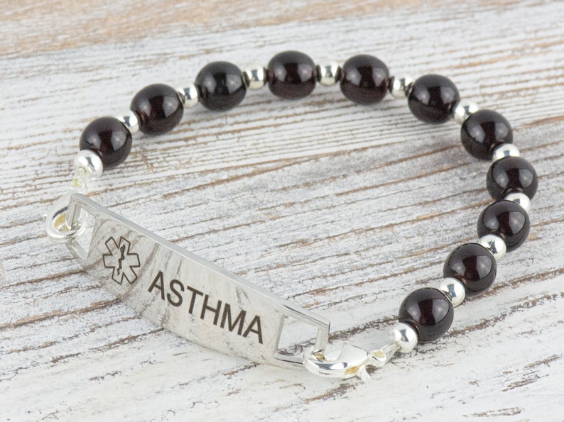 K&ouml;nnte beinhalten: Ein silbernes medizinisches Armband mit schwarzen Perlen und dem Wort "ASTHMA" auf dem Anh&auml;nger. Der Anh&auml;nger zeigt auch ein medizinisches Symbol.
