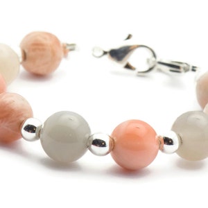 May include: A bracelet made of light pink, white, and gray moonstone beads with silver spacers and a silver clasp.