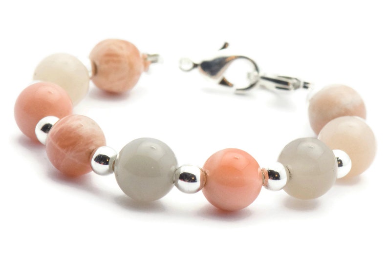 May include: A bracelet made of light pink, white, and gray moonstone beads with silver spacers and a silver clasp.