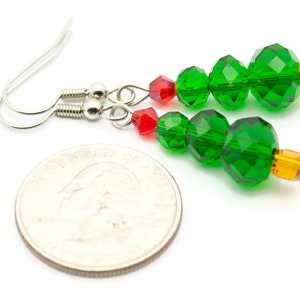 May include: A pair of green and red Christmas tree earrings with silver hooks. The earrings are made with faceted glass beads and are about the size of a quarter.