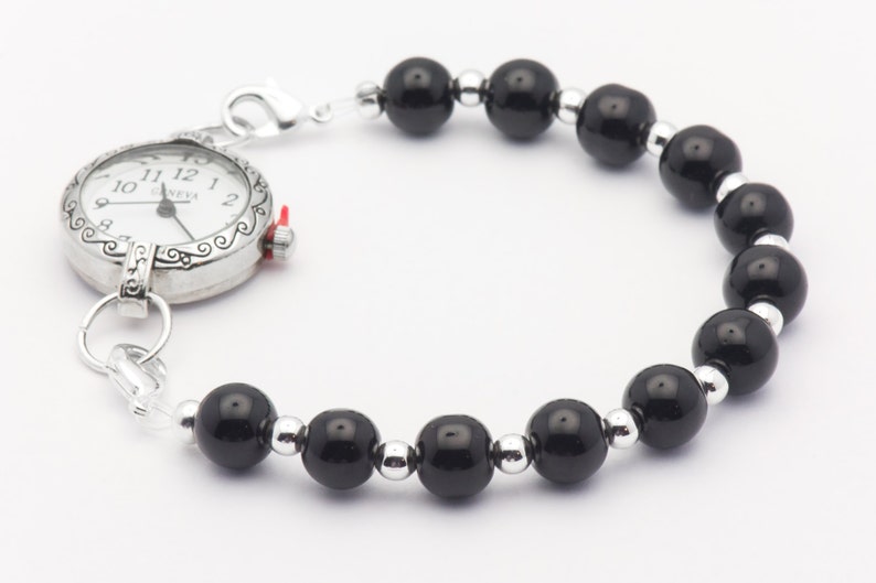 May include: A silver pocket watch with a black beaded chain. The watch face has black Roman numeral hour markers and a silver second hand.
