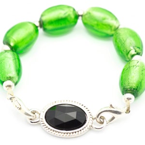 May include: A green glass bead bracelet with a silver clasp and a black gemstone. The bracelet is made of oval-shaped beads with a silver accent on each bead.