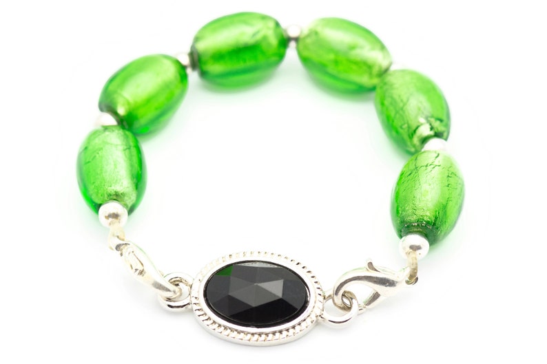 May include: A green glass bead bracelet with a silver clasp and a black gemstone. The bracelet is made of oval-shaped beads with a silver accent on each bead.