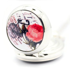Puede incluir: Un medall&oacute;n plateado con fondo blanco y una imagen vintage de una bicicleta y una rosa rosa. El medall&oacute;n tiene una cadena plateada.