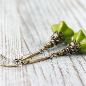 Puede incluir: Un par de pendientes colgantes verdes y dorados con un dise&ntilde;o de flor. Los pendientes est&aacute;n hechos con una flor de cer&aacute;mica verde y detalles met&aacute;licos dorados.