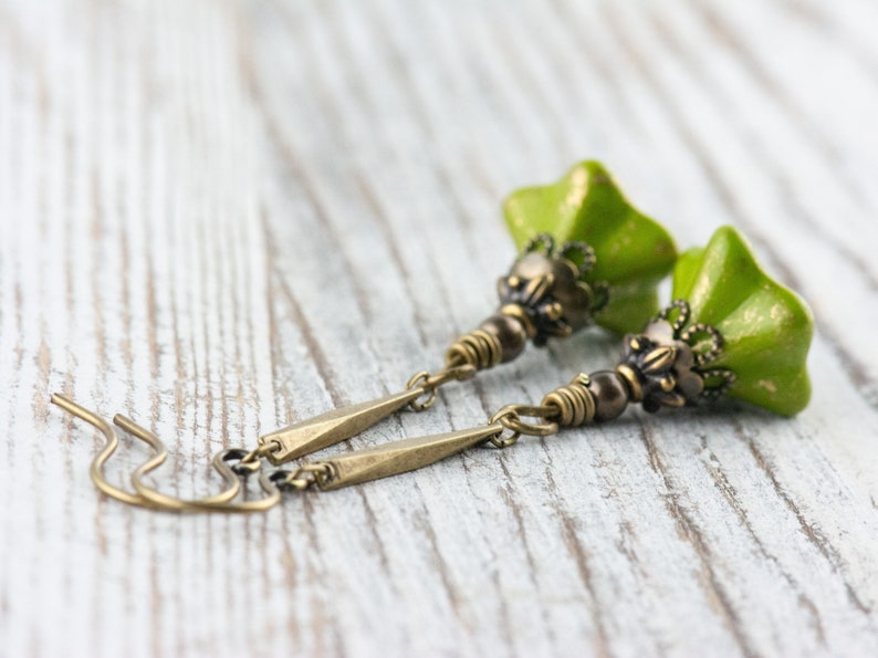 Puede incluir: Un par de pendientes colgantes verdes y dorados con un dise&ntilde;o de flor. Los pendientes est&aacute;n hechos con una flor de cer&aacute;mica verde y detalles met&aacute;licos dorados.