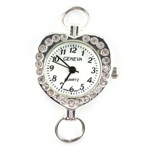 Pu&ograve; includere: Orologio a forma di cuore argentato con quadrante bianco e dettagli in strass. Il quadrante dell'orologio riporta la scritta "GENEVA QUARTZ".