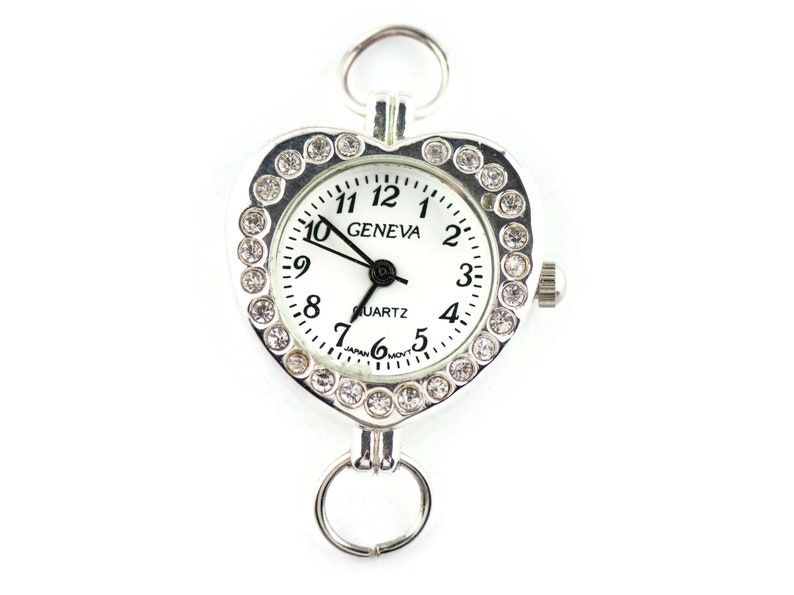 Pu&ograve; includere: Orologio a forma di cuore argentato con quadrante bianco e dettagli in strass. Il quadrante dell'orologio riporta la scritta "GENEVA QUARTZ".