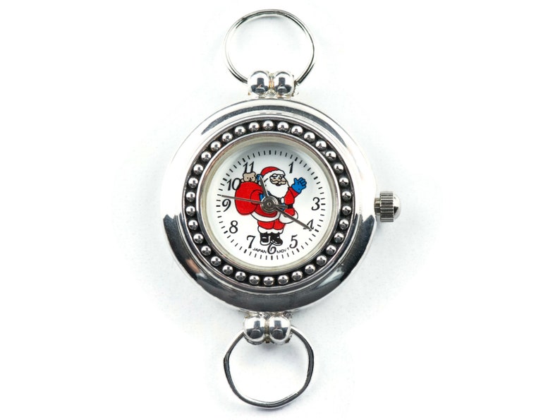 Puede incluir: Un reloj de bolsillo plateado con una esfera blanca y un dise&ntilde;o de Pap&aacute; Noel. El reloj tiene un bisel con cuentas y una cadena unida a la parte superior.