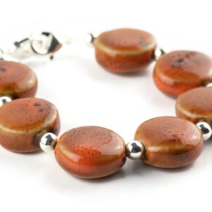 May include: A bracelet made of brown ceramic beads with silver accents. The beads are round and have a speckled texture.