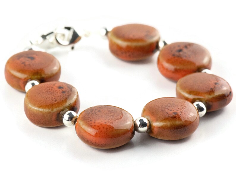 May include: A bracelet made of brown ceramic beads with silver accents. The beads are round and have a speckled texture.
