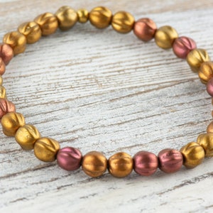 May include: A gold and copper beaded bracelet with a graduated color pattern. The beads are round and have a textured surface.