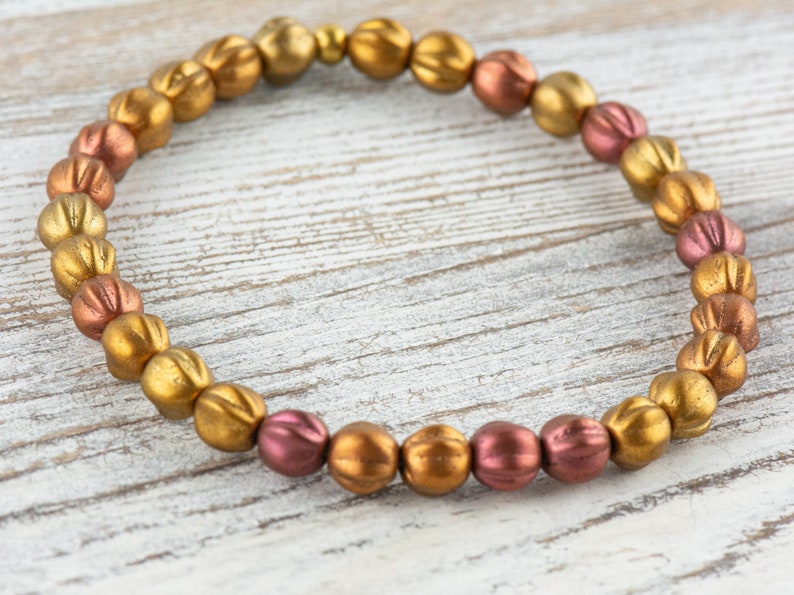 May include: A gold and copper beaded bracelet with a graduated color pattern. The beads are round and have a textured surface.