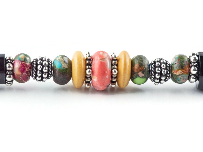 K&ouml;nnte beinhalten: Ein buntes Perlenarmband mit einer Mischung aus braunen, gr&uuml;nen, rosa und gelben Perlen. Das Armband hat silberne Akzente und schwarze Endkappen.