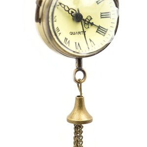 May include: A gold-toned pocket watch with Roman numeral markings on the face and a chain attached to a bell-shaped pendant.