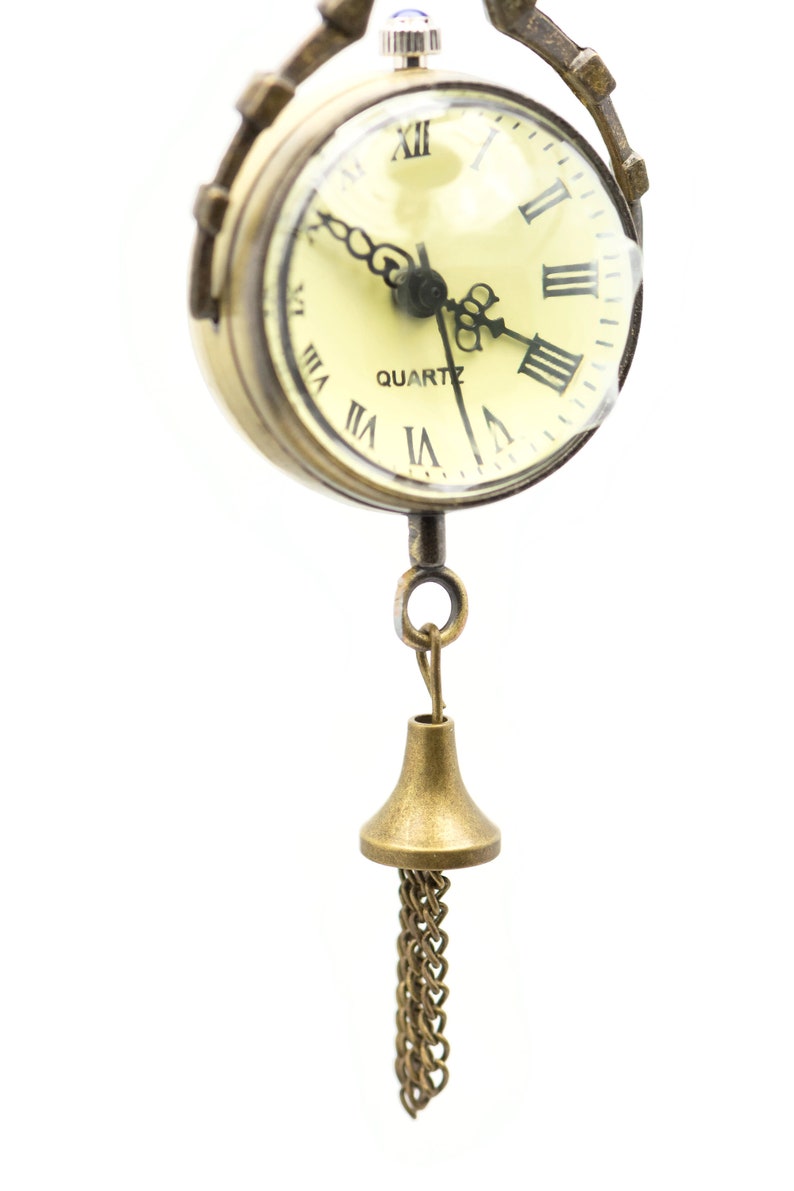 May include: A gold-toned pocket watch with Roman numeral markings on the face and a chain attached to a bell-shaped pendant.