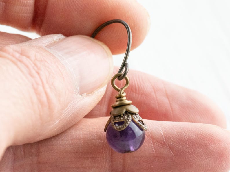 K&ouml;nnte beinhalten: Einzelner Amethyst-Ohrring mit antikfarbener Messing-Filigran-Kappe und Ohrhaken. Der Ohrring hat einen kleinen, runden, polierten, lila Edelstein. Die Metallkomponenten haben ein gealtertes, Vintage-Aussehen.