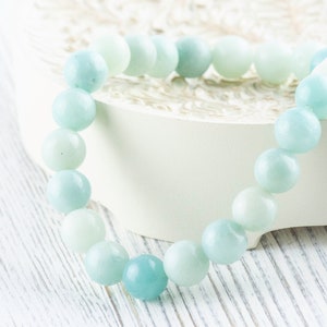 May include: A light blue gemstone bracelet with round beads. The bracelet is on a white surface.