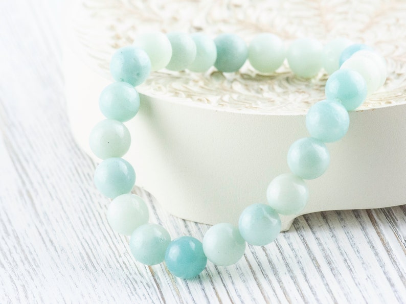 May include: A light blue gemstone bracelet with round beads. The bracelet is on a white surface.